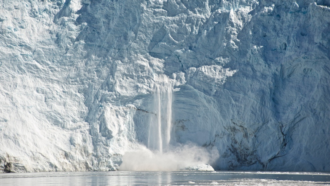 Mitten aus einer weißen Gletscherfront ergießt sich ein Wasserfall.