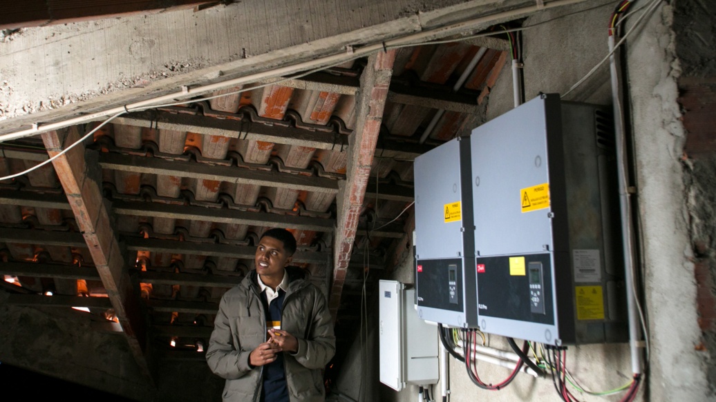 Alekson Dias da Luz steht auf dem Dachboden, vor ihm die Transformatoren der Photovoltaikanlage.