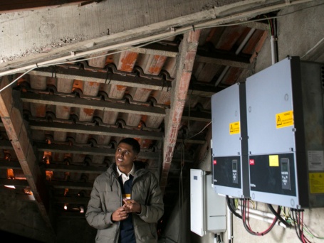 Alekson Dias da Luz steht auf dem Dachboden, vor ihm die Transformatoren der Photovoltaikanlage.