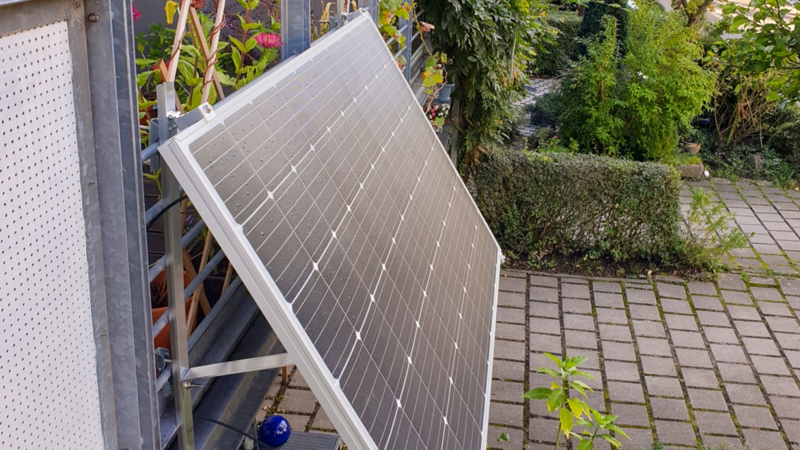 Ein Solarpanel ist mit einer Metallkonstruktion an einem Balkongeländer fixiert. 
