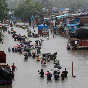In einer überfluteten Straße laufen Menschen mit Regenschirmen durch das hüfthoch stehende Wasser, Lastwagen stehen quer