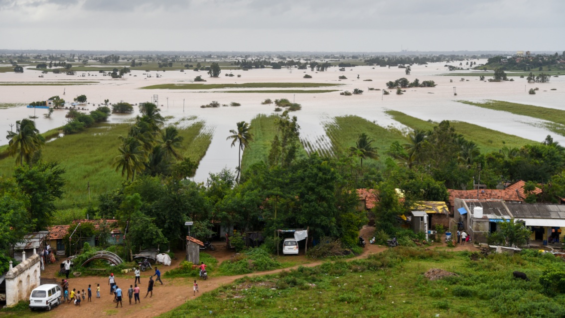 Eine Fläche mit Feldern und Häusern ist weitläufig überschwemmt. Einige höher gelegene Häuser stehen im Trockenen.