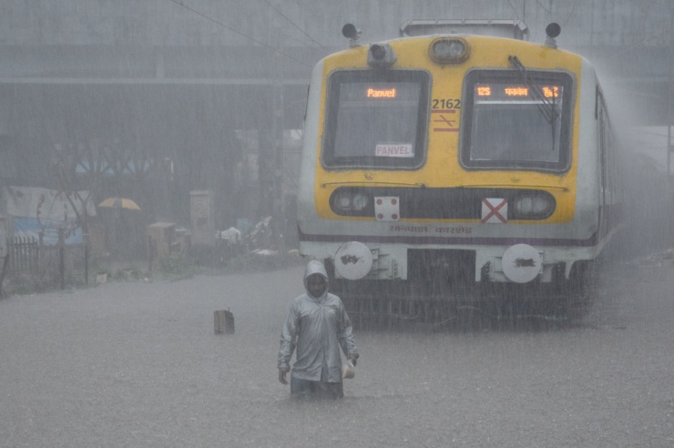 Ein Zug steht im Monsunregen, das Gleisbett ist komplett überflutet. Davor steht ein Mann knietief im Wasser.