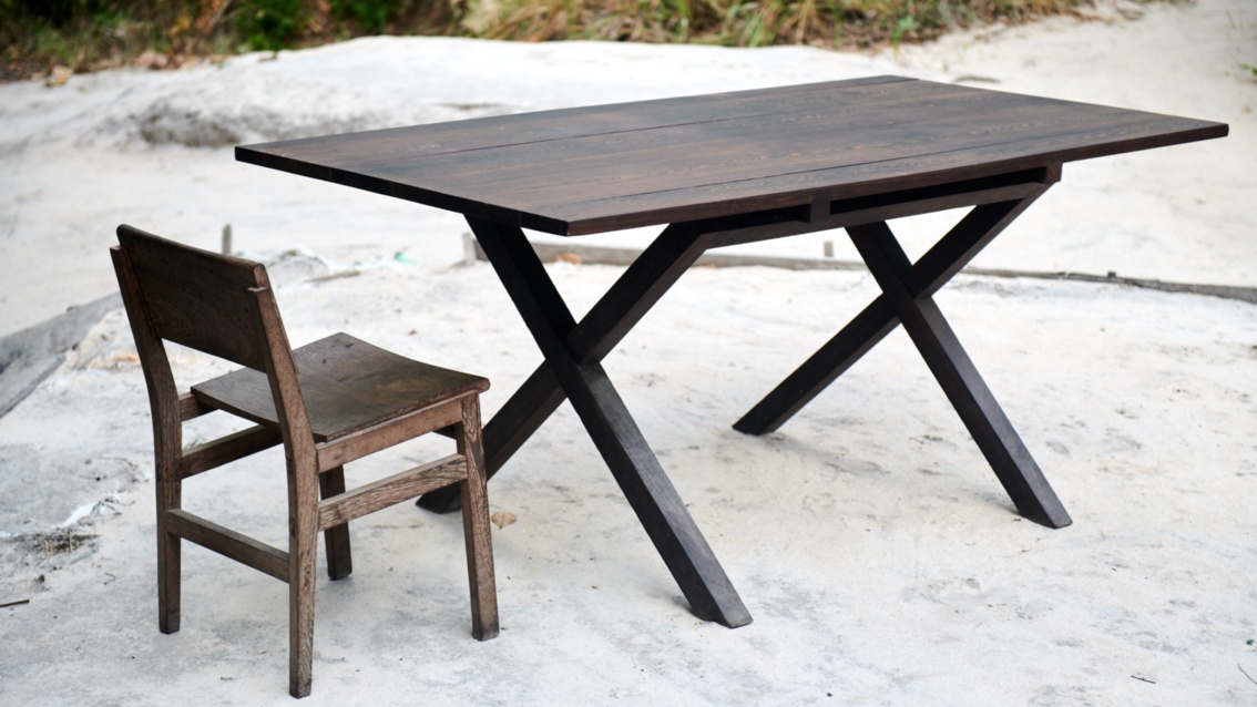 Ein Stuhl aus dunklem Holz steht an einem eleganten Holztisch mit gekreuzten Beinen. 