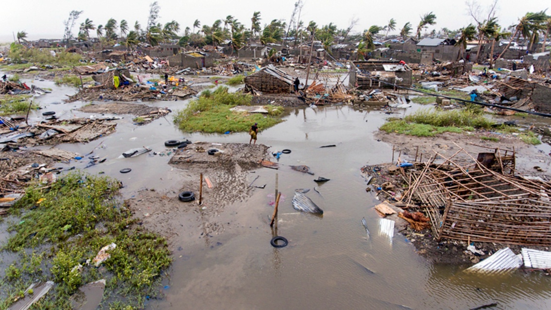 Eine überflutete und zerstörte Stadt: Zwischen eingestürzten Häusern und Trümmern waten Menschen durchs Wasser. 