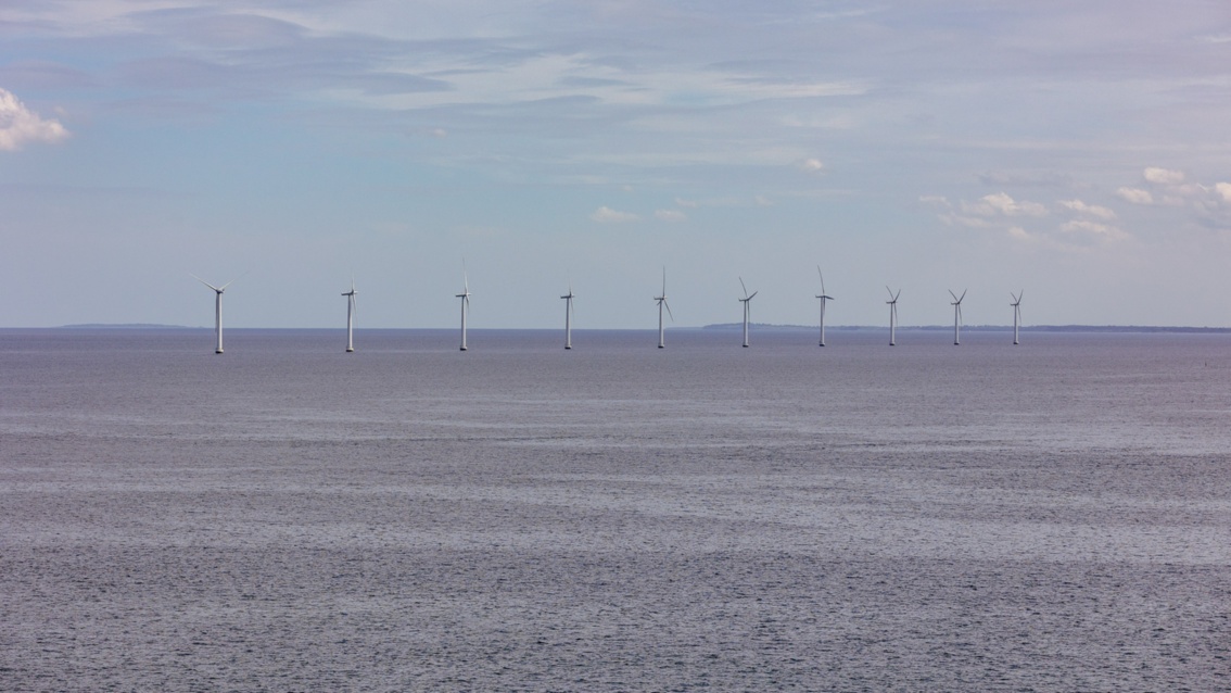 Off the coast, ten wind turbines stand on small piers in the sea - the water looks gray and rugged.