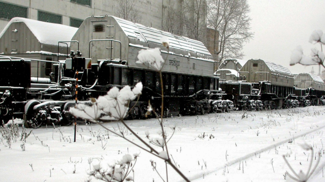 Das Schwarzweißfoto zeigt einen mit hellen Metallcontainern beladenen Zug  in einer winterlichen Landschaft.