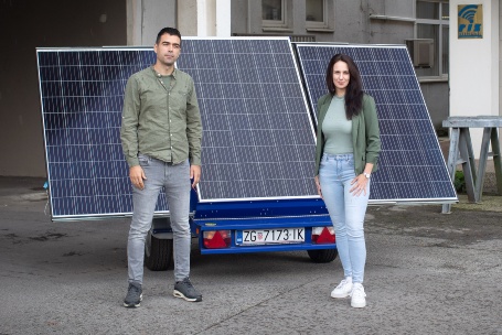 Vor einem Solar-Modul, das auf einen Anhänger montiert ist, stehen ein junger Mann und eine junge Frau und schauen freundlich in die Kamera.