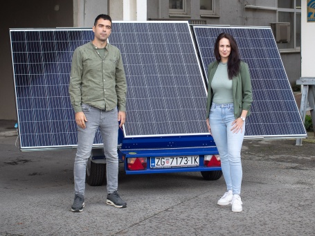 Vor einem Solar-Modul, das auf einen Anhänger montiert ist, stehen ein junger Mann und eine junge Frau und schauen freundlich in die Kamera.