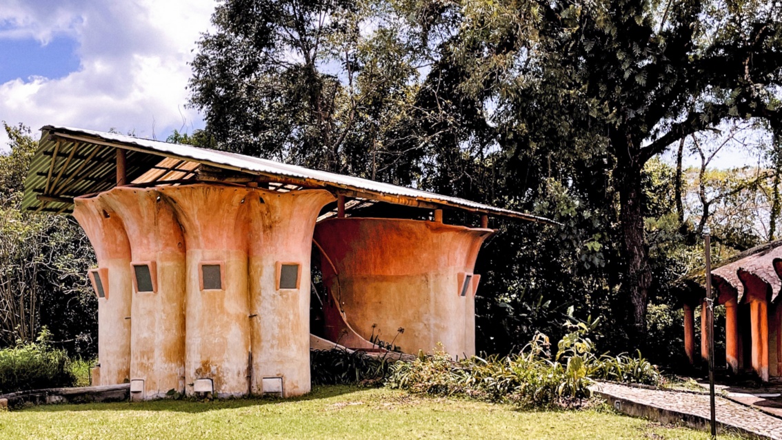 Eine Lehmhütte mit Wellblechdach: durch die organische Form der rötlichen Wände ähnelt sie einem Pilz.