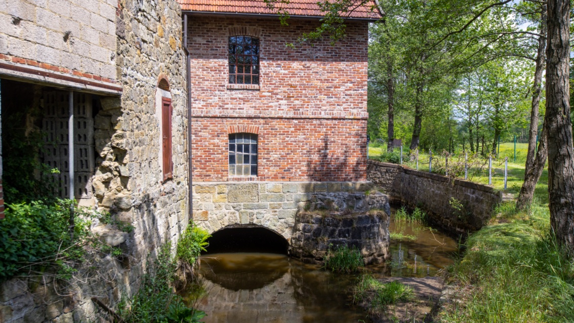 Eine historische Wassermühle aus Sandstein mit Klinkeranbau: Wassergräben verlaufen unter und neben dem Gebäude.