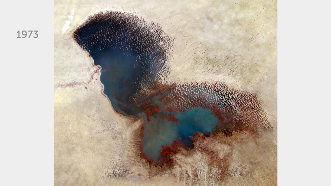Eine farbveränderte Satellitenaufnahme zeigt einen großen See, der sich klar von angrenzenden Steppen und Wüsten abhebt.   
