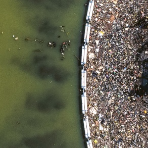 Vogelperspektive: An einer schwimmenden Barriere auf einem Gewässer hat sich Plastikmüll gesammelt. 