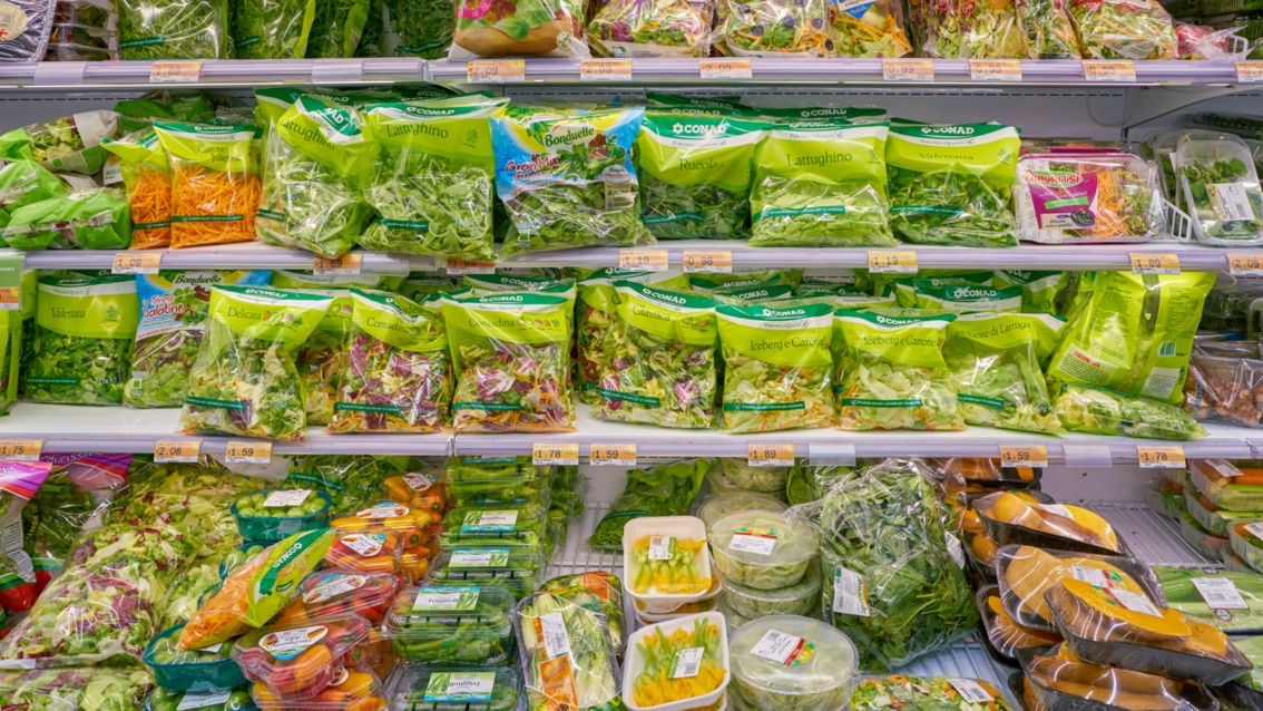 Ein hell erleuchtetes Kühlregal voller Salat und Gemüse, eingepackt und verschweißt in Kunststoff. 