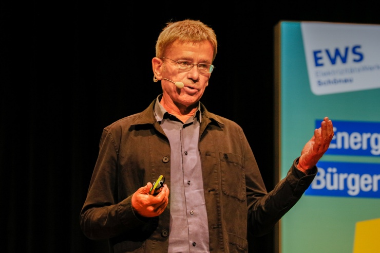 Ein Mann mit grau meliertem Haar und rahmenloser Brille hält einen Vortrag auf der Bühne. 