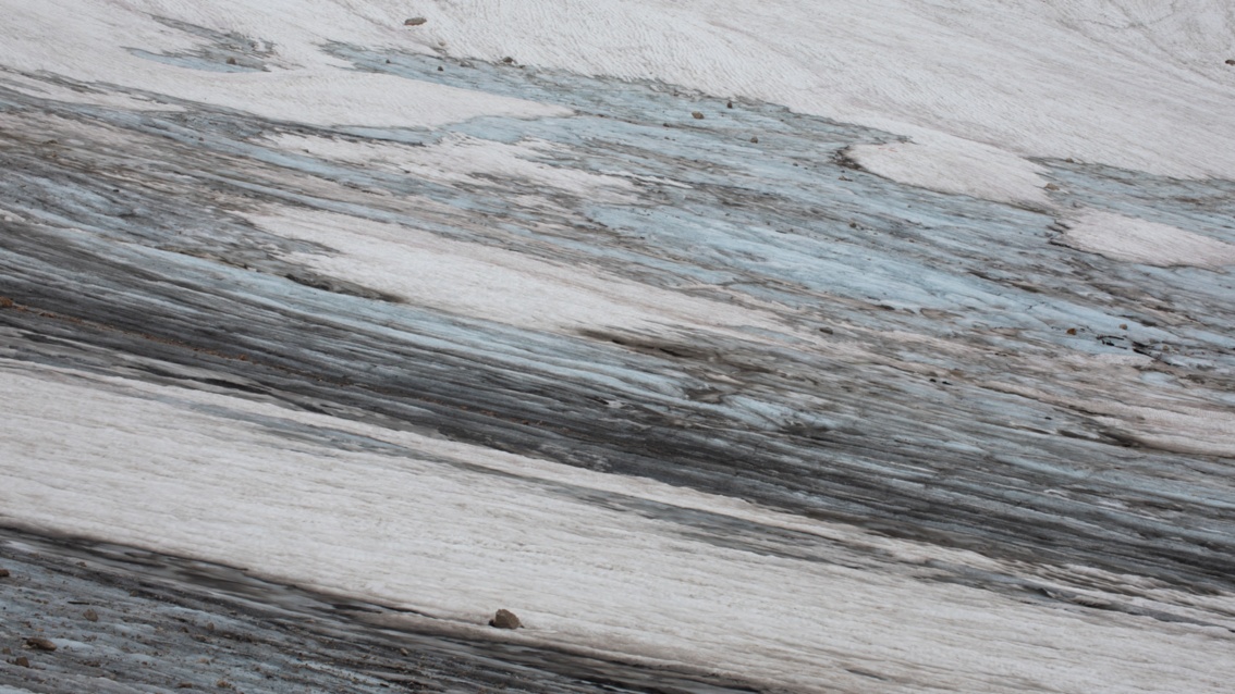 Blick auf einen Hang: Schmutzig-weißes Eis schimmert stellenweise hellblau und wird von dunkelgrauen Schlieren durchzogen.