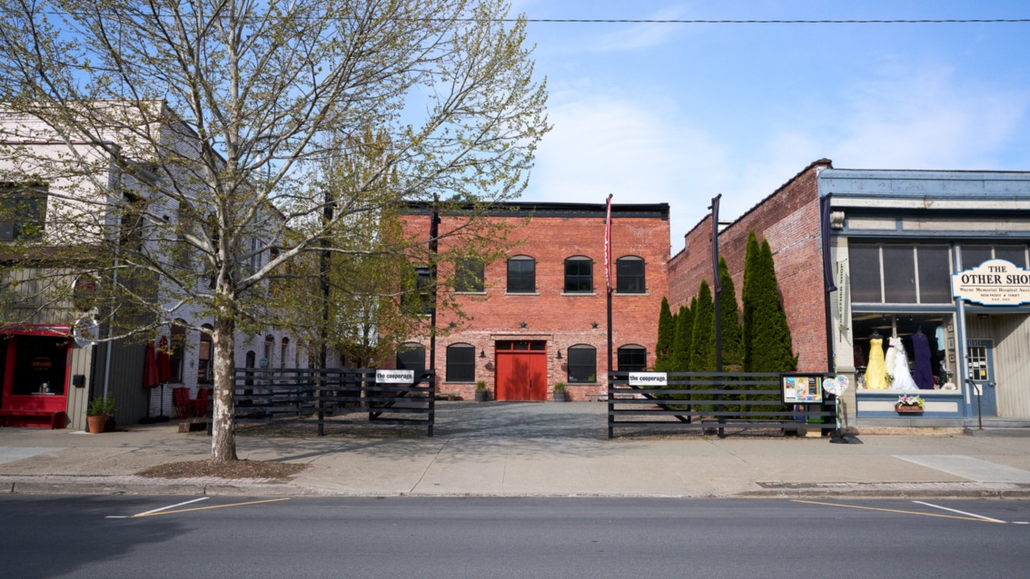 Ein Backsteinhaus mit breiten Fenstern und rotem Tor steht leicht versetzt, in zweiter Reihe zu den anderen Häuser. 