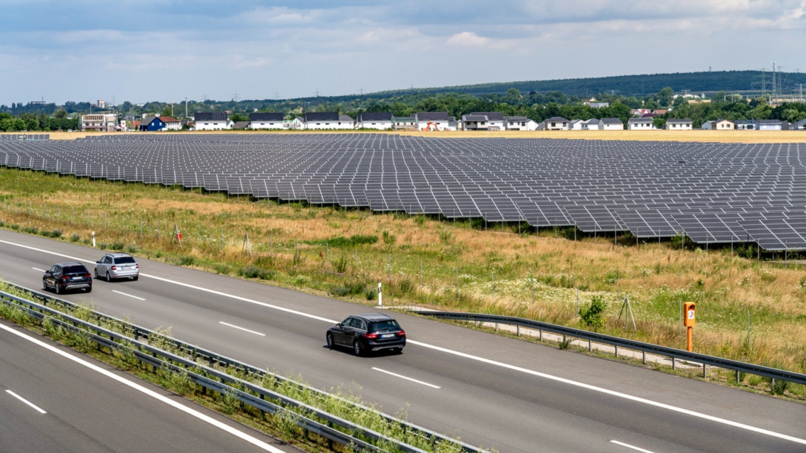 Ein Solarpark erstreckt sich seitlich neben einer Autobahn – nur ein kleiner Grünstreifen trennt PV-Module und Fahrbahn.