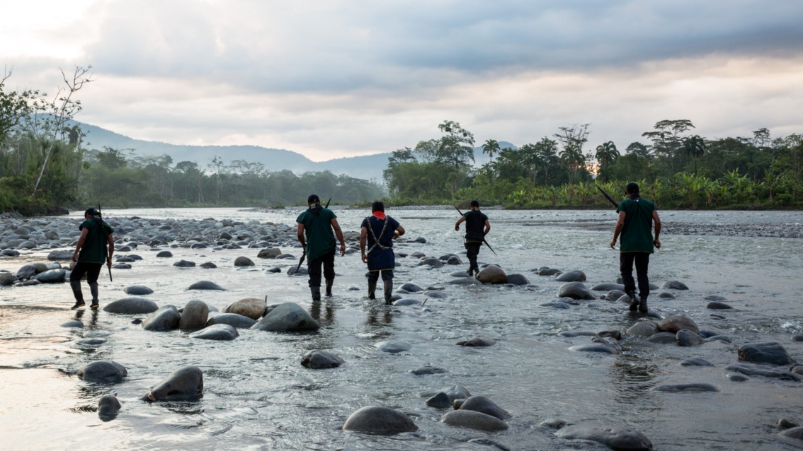 Fünf Männer der Patrouille waten zwischen kugelförmigen Steinen durch das Wasser eines Flusses.