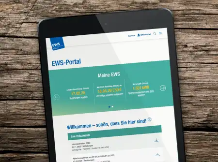 Auf einem groben Holztisch ein schwarzes Tablet, sie aufgerufene Website ist die Start- und Willkommensseiteite des EWS-Portals