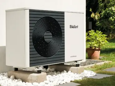 Am Balkon eines mit reichlich Pflanzen geschmückten Balkons ist eine Balkon-PV-Anlage montiert. Im Hintergrund eine Backsteinmauer.