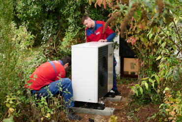 Zwei Monteure installieren eine Wärmepumpe im Garten