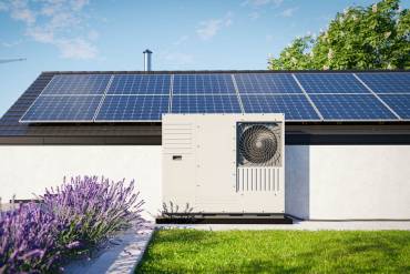 Modernes Haus mit Photovoltaik auf dem Dach und davor stehender Wärmepumpe