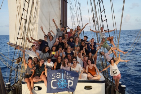 Eine Gruppe gutgelaunter junger Menschen auf dem Deck eines Segelschiffs, vor ihnen ein Banner mit der Aufschrift «Sail to the COP»