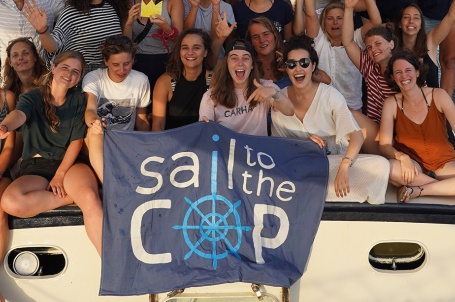 Eine Gruppe gutgelaunter junger Menschen auf dem Deck eines Segelschiffs, vor ihnen ein Banner mit der Aufschrift «Sail to the COP»