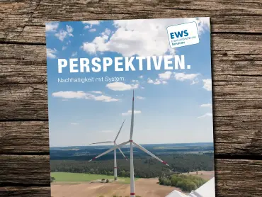 Auf einem Holztisch eine Broschüre mit dem Foto von Windkraftanlagen, Titel: Perspektiven – Nachhaltigkeit mit Systen