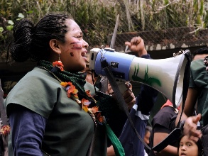 Eine indigene Frau mit Gesichtsbemalung spricht in eine Megafon