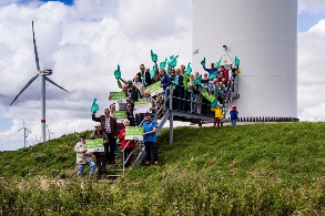 Gruppe von Menschen mit Protestplakaten steht am Fuß einer Windkraftanlage