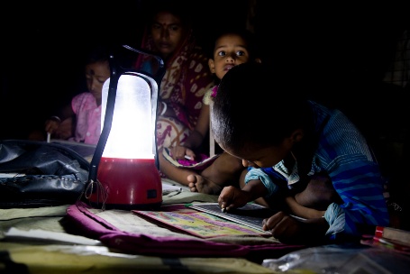 Eine Familie mit drei Kindern sitzt im Schein einer Solarlampe in einem ansonsten dunklen Raum, die Kleinen machen Hausaufgaben oder malen.
