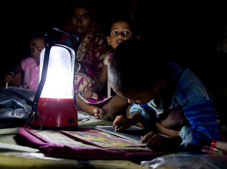Eine Familie mit drei Kindern sitzt im Schein einer Solarlampe in einem ansonsten dunklen Raum