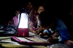 Eine Familie mit drei Kindern sitzt im Schein einer Solarlampe in einem ansonsten dunklen Raum