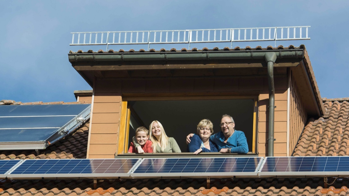 Familie blickt aus Dachgaube auf Photovoltaik-Module