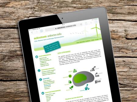 Auf einem Holztisch liegt ein Tablet-Computer, auf dessen Display die Website oekostrom-anbieter.info erscheint.