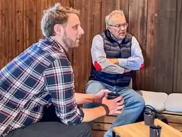 Zwei Personen sitzen im Interview vor einer holzgetäfelten Wand