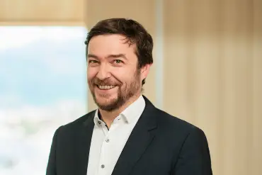 Portrait Sebastian Sladek vor einemFenster und einer holzvertäfelten Wand