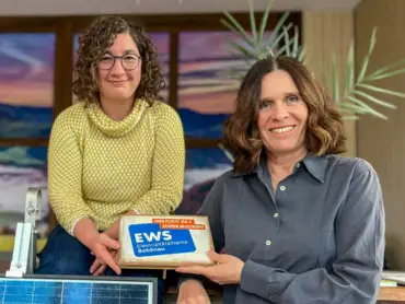 Zwei Mitarbeiterinnen im EWS-Store in Freiburg zeigen einen Tischaudsteller mit EWS-Logo