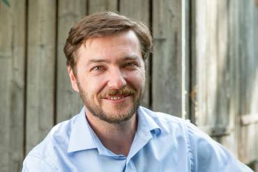 Portrait: Sebastian Sladek vor einer Holzwand