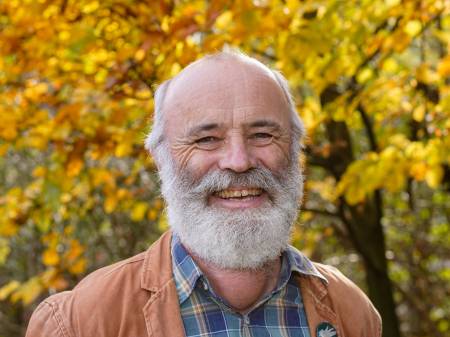 Ulrich Martin Drescher steht vor herbstlichen Laubbäumen und lacht freundlich in die Kamera.
