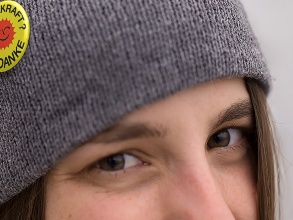 Eine junge Frau schaut verschmitzt in die Kamera; an ihrer grauen Mütze ist ein Atomkraft-neine-danke-Anstecker befestigt. 