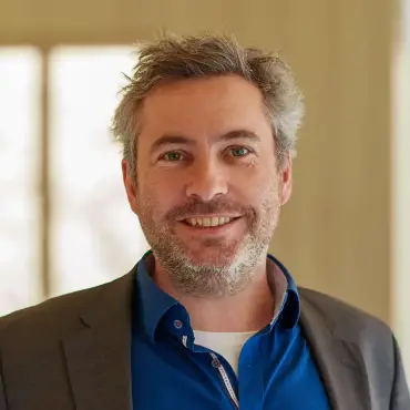 Alexander Sladek in einem Flur, der in lichten Holztönen gehalten ist