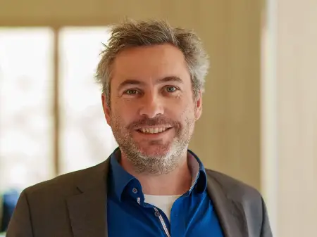 Sebastian Sladek steht, die Hände in die Hüften gestemmt, in einem lichtdurchfluteten Gang.