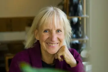 Drei junge Mitarbeitende sitzen auf einer Treppe in einem lichten Gebäude und lächeln in die Kamera.