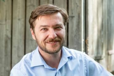 Portrait: Sebastian Sladek vor einer Holzwand