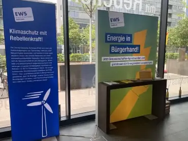 Zwei Infotafeln zu Klimaschutz und Energie in Bürgerhand vor einer Fensterfront zur Straße