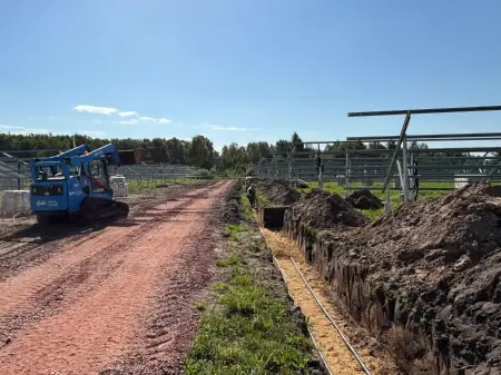 Gestelle für die Montage von PV-Modulen, ein Bagger sowie ein Graben, in dem Leitungen liegen