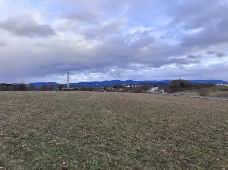 Eine brachliegende Landwirtschaftsfläche, im Hintergrund ein schraubenartig verkleideter Turm und bewaldete Höhenzüge